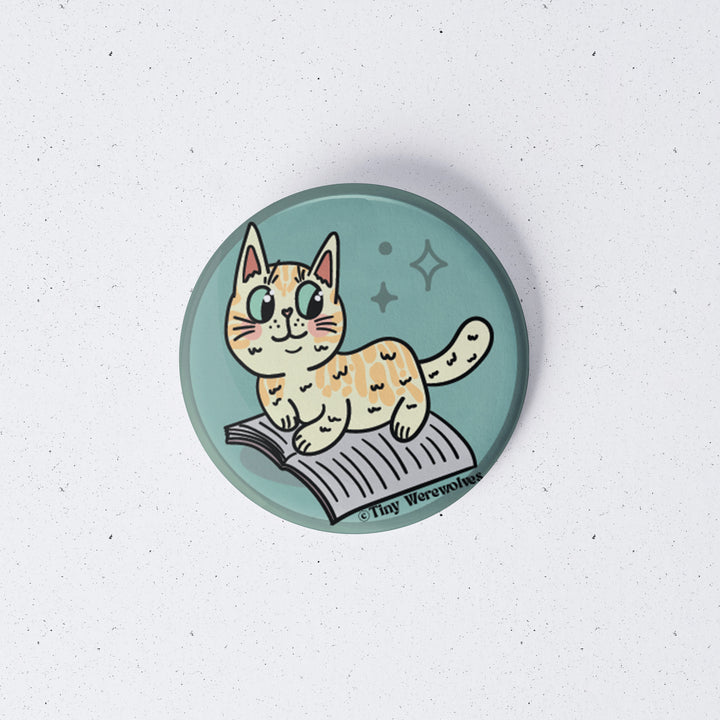 Based in Chicago by queer artist & designer Kayla Pekkala - Tiny Werewolves | Orange Book Cat 1" Mini Button Pin in | Shop to get your Metal Pinback Button with collections featuring retro-inspired designs infused with social commentary art, highlighting modern social & current events.