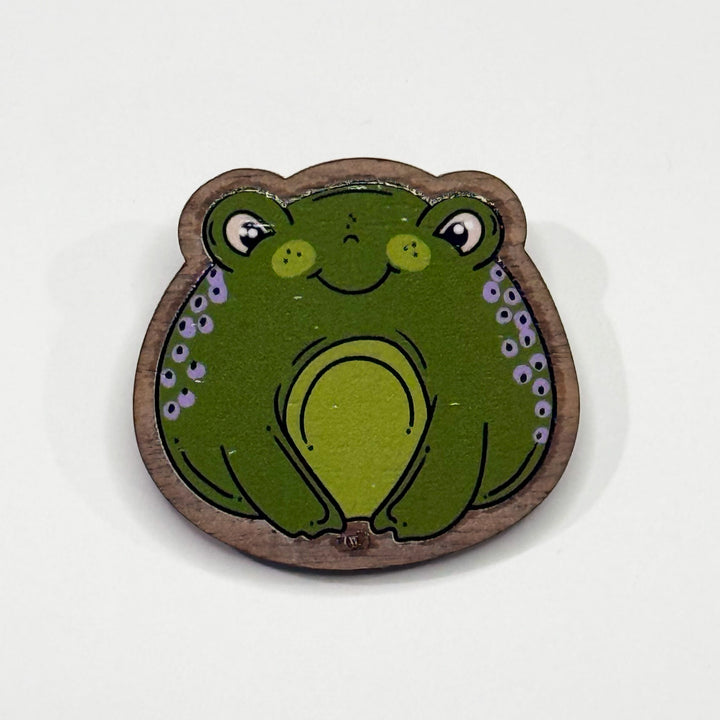 Based in Chicago by queer artist & designer Kayla Pekkala - Tiny Werewolves | Frog Wood Pin in Walnut | Shop to get your Wood Pin with collections featuring retro-inspired designs infused with social commentary art, highlighting modern social & current events.