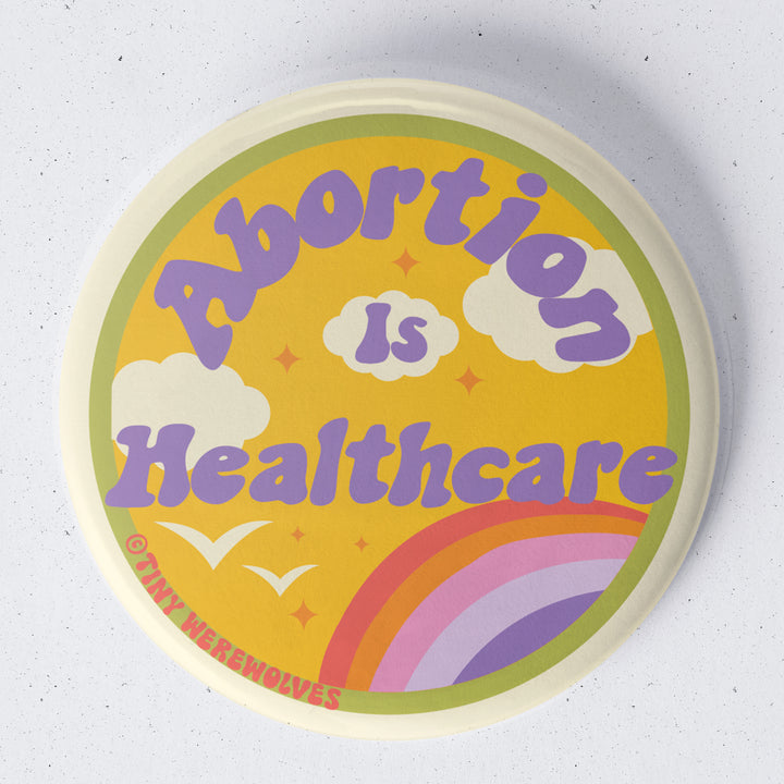 Based in Chicago by queer artist & designer Kayla Pekkala - Tiny Werewolves | Abortion Is Healthcare 1.75" Button Pin in | Shop to get your Metal Pinback Button with collections featuring retro-inspired designs infused with social commentary art, highlighting modern social & current events.
